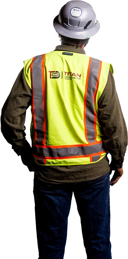 A person wearing a hard hat, a yellow reflective safety vest with the "Titan" logo and jeans stands with their back to the camera, representing Titan's commitment to quality Commercial Dock and Door Solutions.
