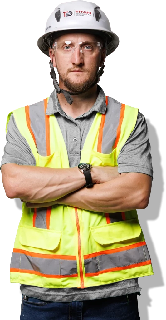 A construction worker wearing a hard hat, safety glasses, and a high-visibility vest stands with arms crossed, representing expertise in Commercial Dock and Door Solutions while looking directly at the camera.